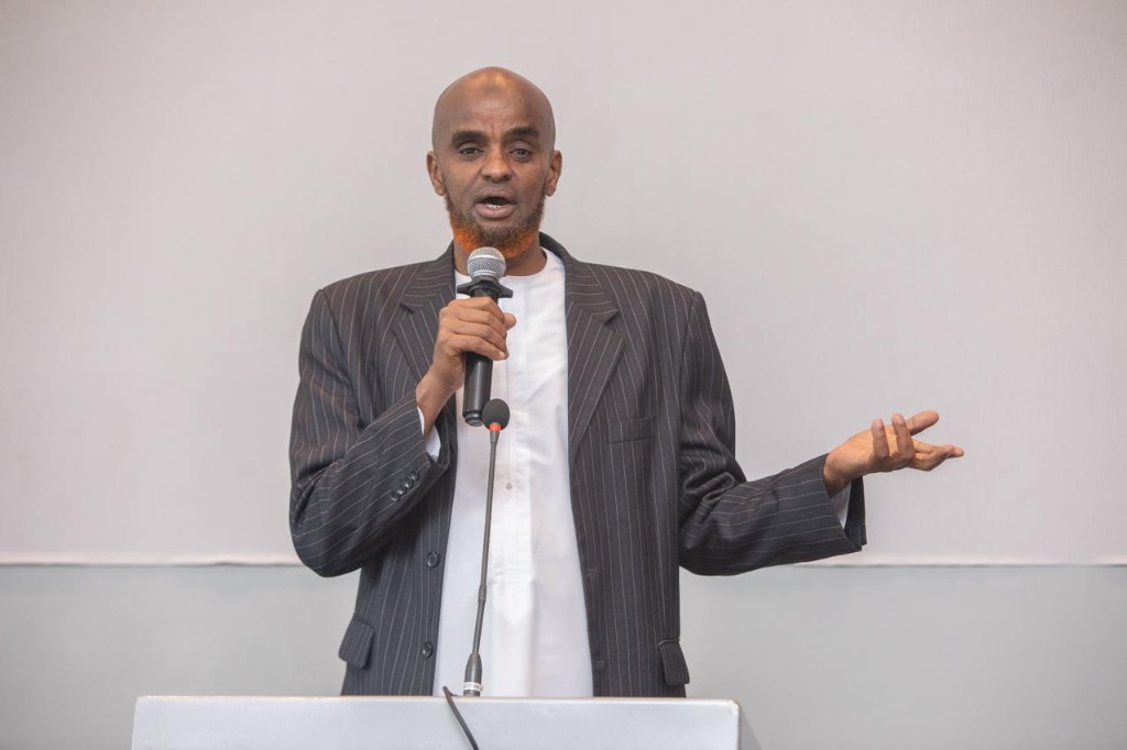 Abdi Ahmed gesturing while speaking at a silver podium