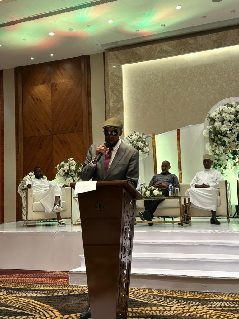 Abdi Ahmed at a wooden podium on a white stage with seated guests