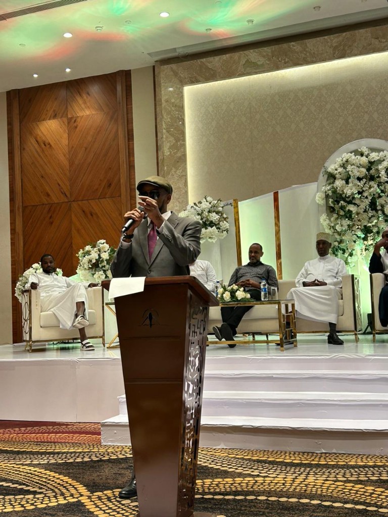 Abdi Ahmed on stage addressing guests seated behind him
